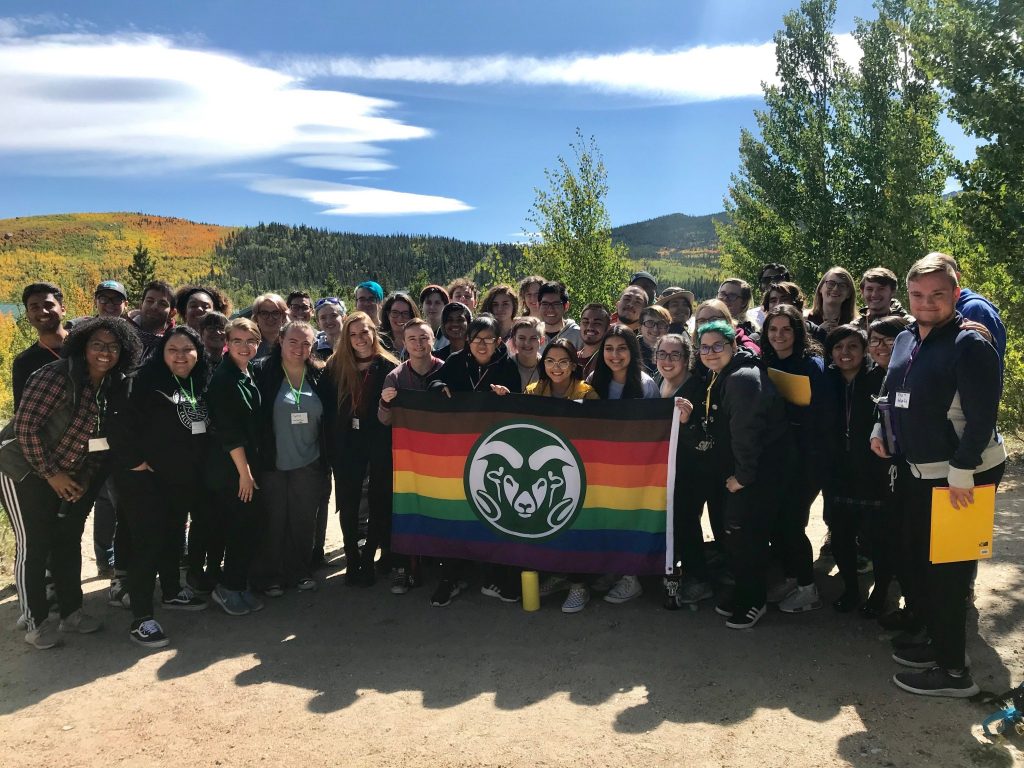 group photo of CSU students with Rainbow Ram pride flag with mountains behind them